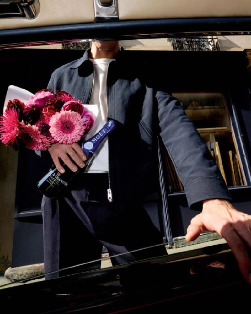 **Translation:** Person stepping out of a car holding a pink bouquet and a bottle of Moët & Chandon Midnight Blue champagne